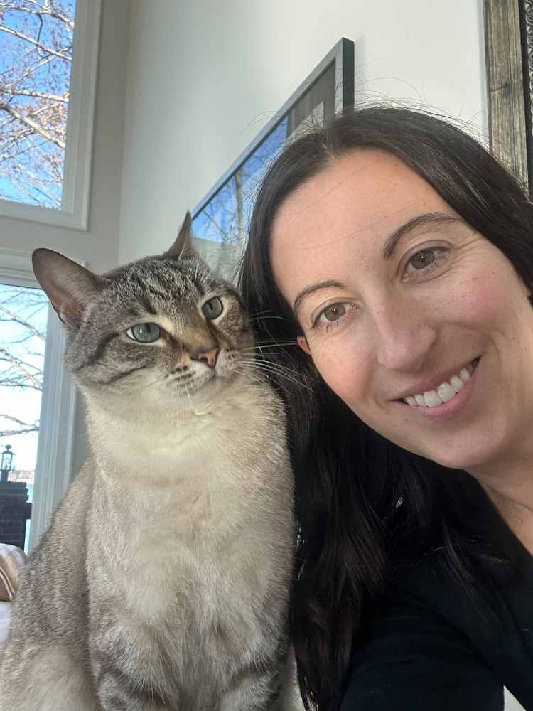A smiling woman sits beside a content cat